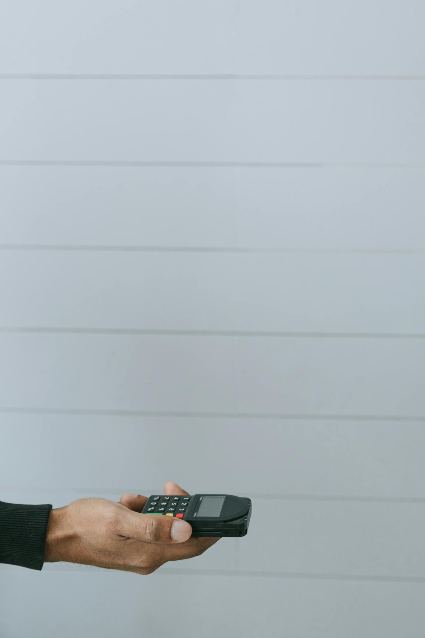 A hand holds a payment terminal against a light background with ample copy space.